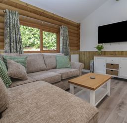 A living room with a beige sofa with green pillows a wooden coffee table and a white cabinet with a television on the wall at Redwood Lodge in Ellesmere