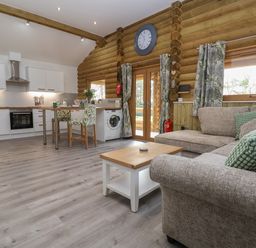 An open plan living area with a sofa coffee table kitchen area and dining chairs at Redwood Lodge in Ellesmere