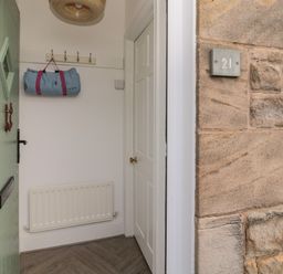 A partially open green door showing a hallway with coat hooks a rolled bag radiator and a white door at Cosy Cottage in Amble