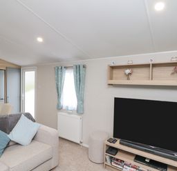 A living room with a sofa, television, shelving unit, curtains, and a refrigerator at Rowan Court 2 in Cayton