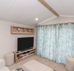 A small living room with a television on a wooden stand and patterned blue curtains at Rowan Court 2 in Cayton