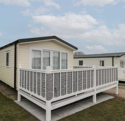 A beige mobile home with a white and grey fenced porch on a grassy area at Rowan Court 2 in Cayton