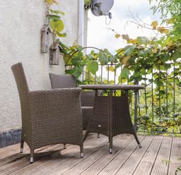 An outdoor balcony with two wicker chairs and a wicker table with climbing plants on the railing at Sea View in St Austell