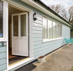 An open white door leading into a house with blue siding two blue chairs on a concrete path and grass at 1 The Dell in Mundesley