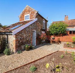 A garden area with gravel and paved patio with table and chairs next to a brick and flint cottage at Admiral Cottage in Blaxhall near Snape Suffolk