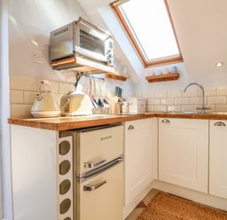 A kitchen with wooden countertops white cabinets a small fridge toaster kettle microwave and a skylight window at Admiral Cottage in Blaxhall near Snape Suffolk