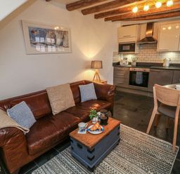 A living area with a brown leather sofa next to a small wooden table and an open kitchen with dining table and chairs at Mulberry Tree in Appledore