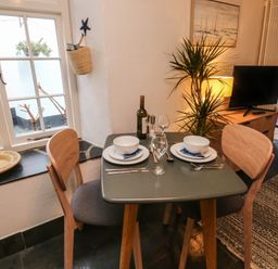 A dining table set for two with plates bowls glasses and cutlery next to a window and a plant in a room at Mulberry Tree in Appledore