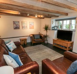 A living room with leather sofas and armchairs a television on a wooden stand and a plant at Pear Tree Cottage in Appledore