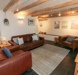 A living room with leather sofas a rug wooden beams on the ceiling and framed pictures on the wall at Pear Tree Cottage in Appledore