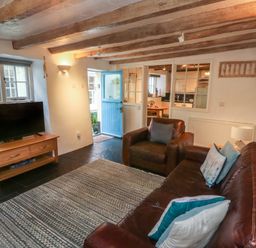 A living room with leather sofa and armchair a wooden TV stand with a television and a blue door at Pear Tree Cottage in Appledore