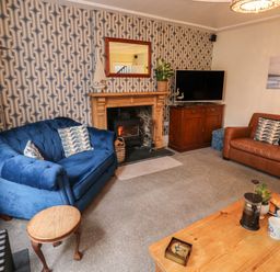 A living room with blue and brown sofas a fireplace with a wood burner and a wooden coffee table at Lands House in Appledore