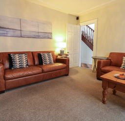A living room with two brown leather sofas a wooden coffee table and paintings on the walls at Lands House in Appledore