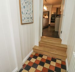 A hallway with checkerboard floor tiles leading to a kitchen with wooden steps at Lands House in Appledore