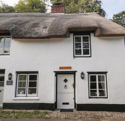 A white thatched cottage with black trim around windows and doors at The Old Thatch in Porlock
