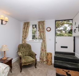 A small room with a green armchair, floral curtains, a side table with a lamp, and a half door with steps at The Old Thatch in Porlock