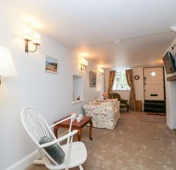 A living room with a white rocking chair a floral sofa a green armchair and a wall mounted television at The Old Thatch in Porlock