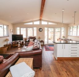 An open plan living room and kitchen with leather sofas and a wood burning stove at Gloccamaura in Bovey Tracey