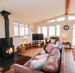 A living room with a wood-burning stove a leather sofa and pillows a television and a wooden floor at Gloccamaura in Bovey Tracey
