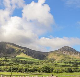 A landscape with green fields trees and mountains under a partly cloudy sky at Caban Cwtch The Cosy Cabin in Llanaelhaearn