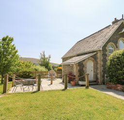 A stone house with a slate roof and a small patio area with chairs and a table surrounded by a garden at St Marks School House Nant-Glas near Rhayader