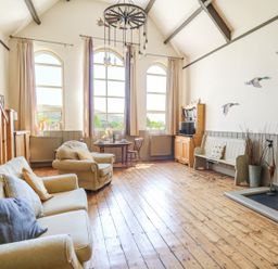 A living room with wooden floors a sofa armchair dining table bookshelf and a fireplace at St Marks School House in Nant-Glas near Rhayader