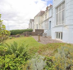 A garden with grass and plants next to a light blue building with large windows and patio furniture at Llys Owen in Criccieth