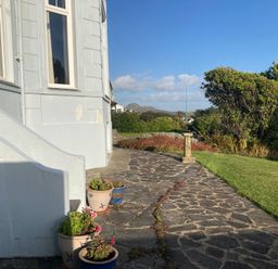 A stone pathway beside a house with potted plants and bushes and a lawn at Llys Owen in Criccieth