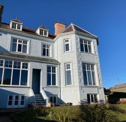 Exterior view of a two story house with multiple windows and a small staircase leading to a door at Llys Owen in Criccieth