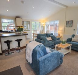 An open living room and kitchen with three blue armchairs a wooden coffee table two black bar stools and a dining table at Hill Top Lodge in Bowness 65 White Cross Bay