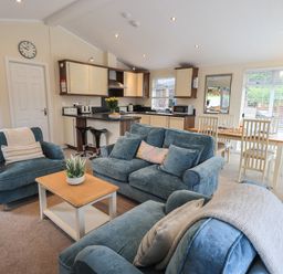 A living area with blue sofas a coffee table and an open kitchen with dining table at Hill Top Lodge Bowness 65 White Cross Bay
