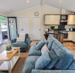 A living room with blue sofa and armchair a wooden coffee table and an open door leading outside at Hill Top Lodge in Bowness 65 White Cross Bay