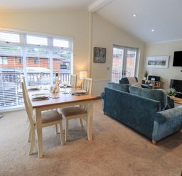 A dining table set for four beside large windows and a living room with blue sofas and a wall mounted TV at Hill Top Lodge in Bowness 65 White Cross Bay