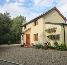 A two-story house with yellow walls and wooden windows surrounded by gravel driveway and plants Rudbaxton Water Rudbaxton near Haverfordwest