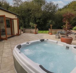 An outdoor patio with a hot tub glass doors and a seating area at Rudbaxton Water in Rudbaxton near Haverfordwest