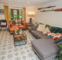 A living room with a gray sectional sofa and a brown leather loveseat near windows with plants at Rudbaxton Water Rudbaxton near Haverfordwest