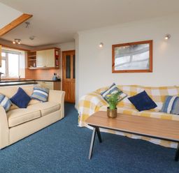A living room with two sofas and a coffee table with flowers and an open kitchen in the background at 5 Seymour Villas in Woolacombe