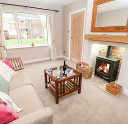 A living room with a beige sofa with cushions a wooden coffee table a wood burning stove and a window at Willows in Corbridge