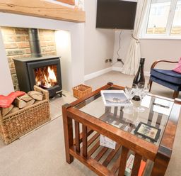 A living room with a wood-burning stove basket of logs glass coffee table bottle of wine and two glasses at Willows in Corbridge