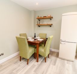 A dining area with a wooden table set for four with green chairs and a cream refrigerator at Willows in Corbridge