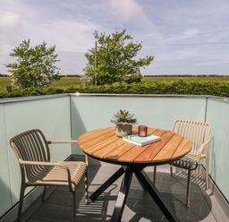 A balcony with a round wooden table two chairs a plant a book and a candle at The Hayloft in Llanfechell