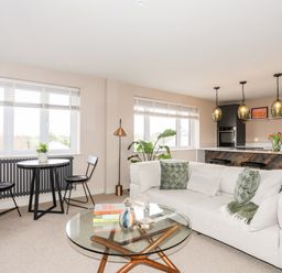 An open living room and kitchen with a round glass coffee table a white sectional sofa with green pillows a small black dining table with two black chairs and three pendant lights at The Hayloft in Llanfechell