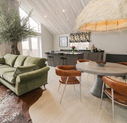 An open living space with a green sectional sofa brown leather chairs a round table and a kitchen island at Garden House in Llanfechell