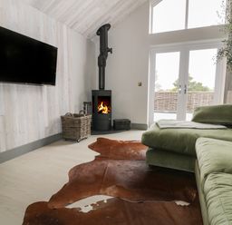A living room with a green sectional sofa a wood stove a wall mounted tv and glass doors at Garden House in Llanfechell