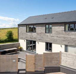 An outdoor patio area with wooden fencing and a dining table next to a two-story house with wooden siding at The Farmhouse in Llanfechell