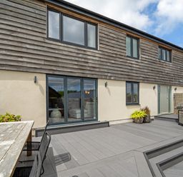 An outdoor patio area with a wooden table and chairs plants a barbecue and a building with multiple windows at The Farmhouse in Llanfechell