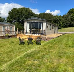 A garden with chairs and a table in front of two mobile homes surrounded by trees at Ambleside in Cullompton