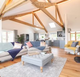 An open living room and kitchen with exposed wooden beams sofas and a wood stove at Trevilges Cottage Trewennack near Helston