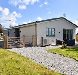 A single story house with a gravel driveway a wooden gate garden furniture and a lawn at The Linhay in Lapford