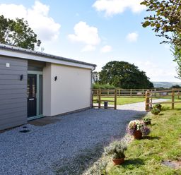 A house entrance with a gravel driveway and a wooden fence with flower pots along the side at The Linhay in Lapford